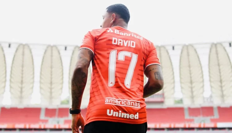 Camisa vermelha com número 17 na cor branca, jogador atacante, David, jogando com a camisa do Inter. A foto é batida pegando o jogador pelas costas, de baixo para cima, talvez em um momento que iria entrar no jogo, substituindo outro jogador. a imagem de fundo é as membranas do estádio Beira-Rio